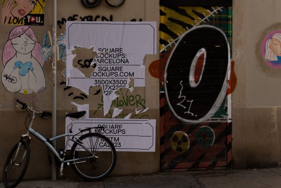 Torn white square poster on weathered wall next to graffiti bike leaning